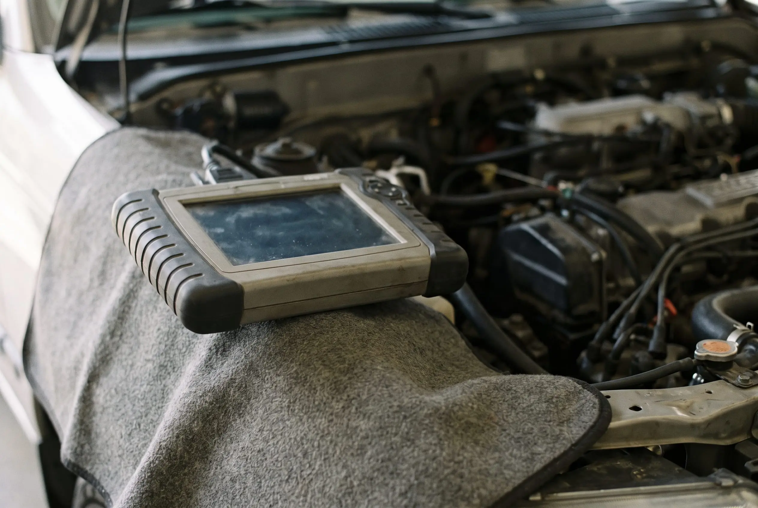 Diagnostic scan tool resting on a fender cover over an engine bay