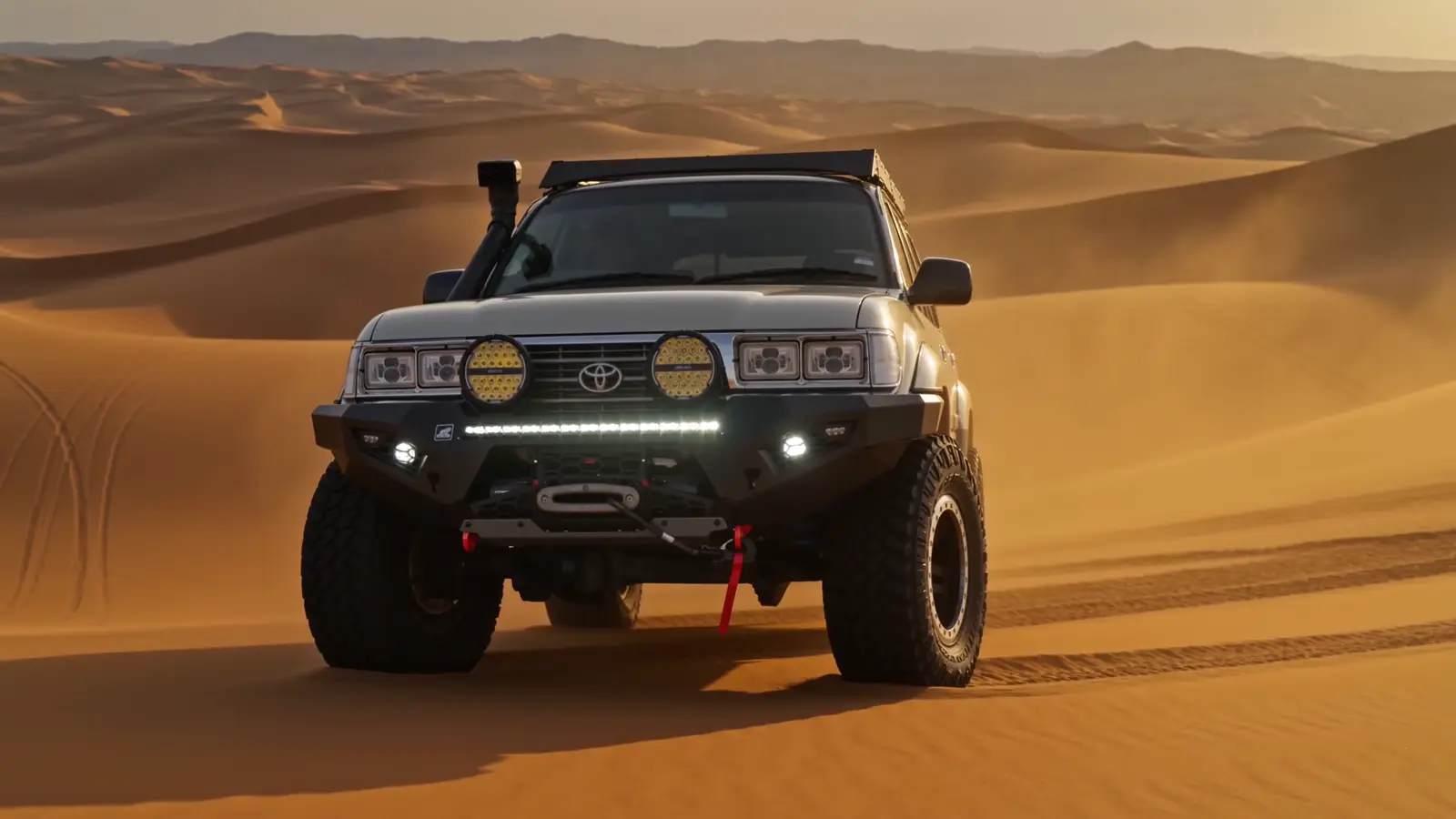 Sand-beige LandCruiser 80 Series touring build with bull bar, snorkel and roof platform at rest in golden desert dunes